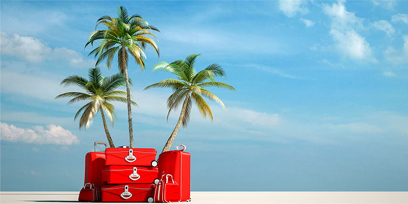 red luggage stacked on the sand in front of palm trees