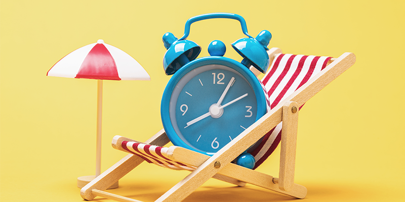 antique alarm clock sitting in beach chair next to a beach umbrella