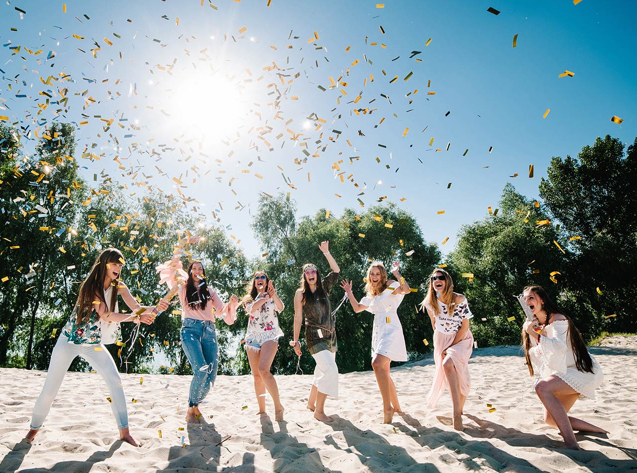 Group of young women throwing confetti on beach