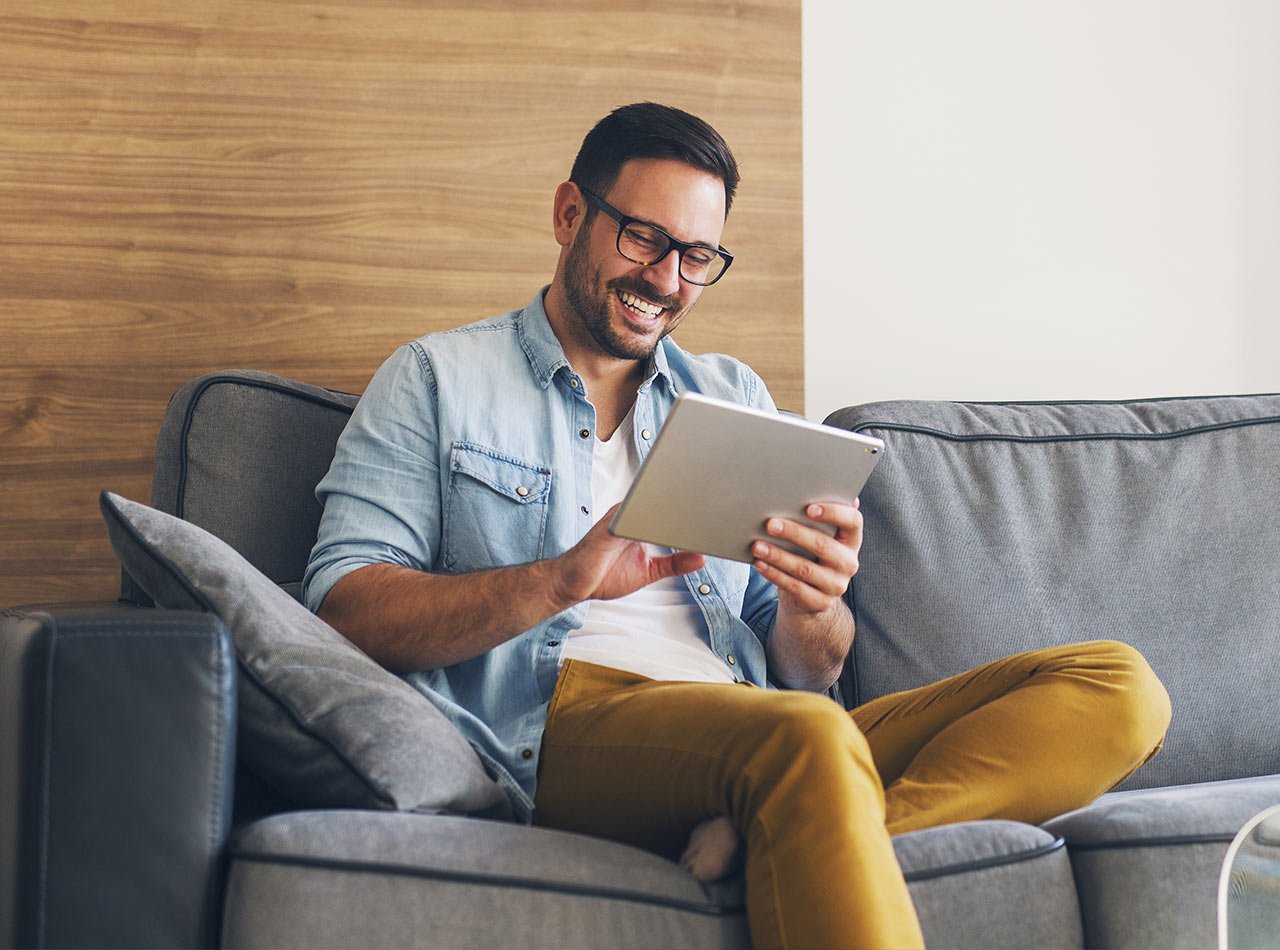 Smiling man sitting on couch and communicating with advisor on a tablet